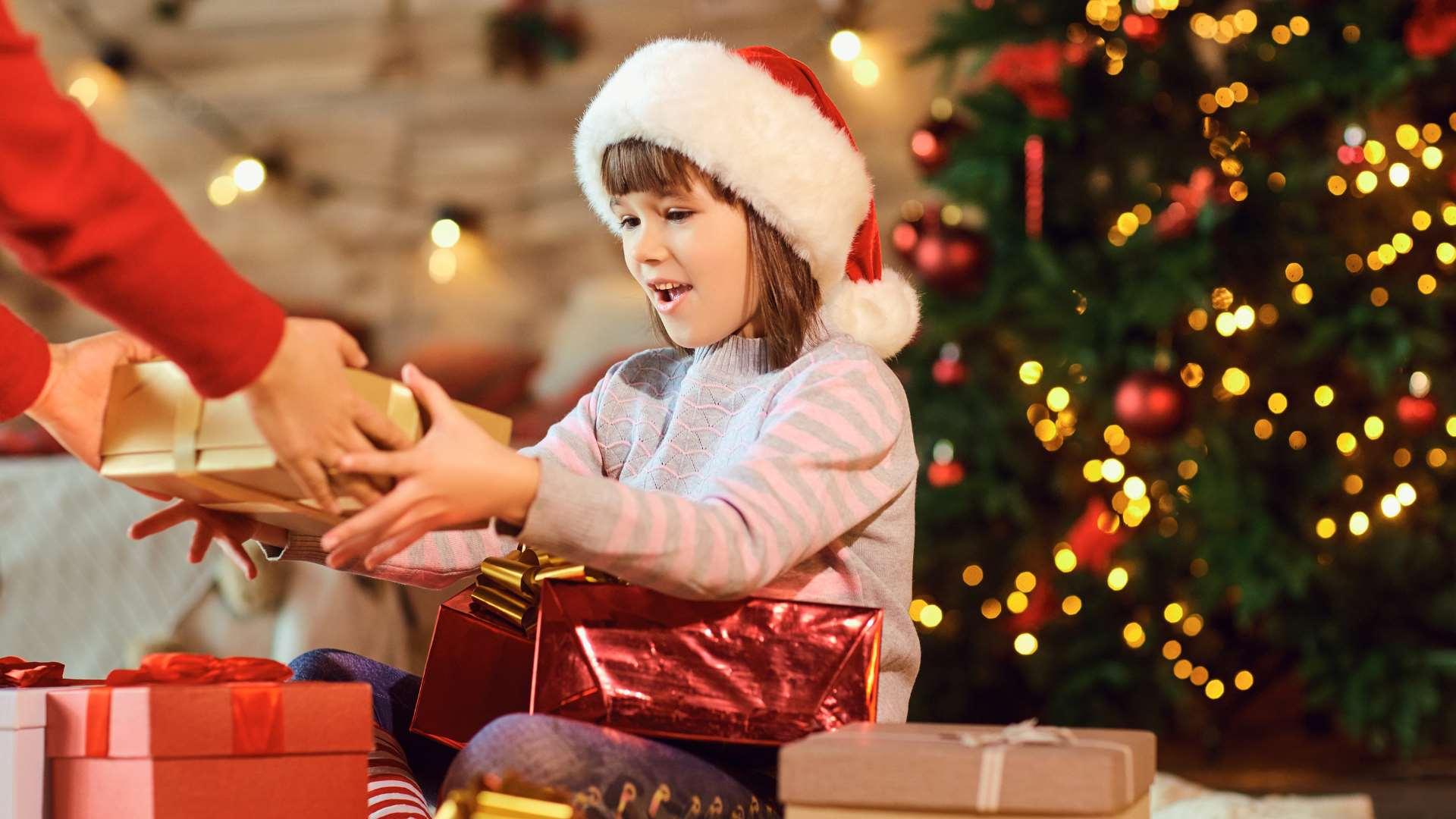 Petite fille avec bonnet de Père Noël qui prend un cadeau, avec un sapin de Noël flou en arrière-plan