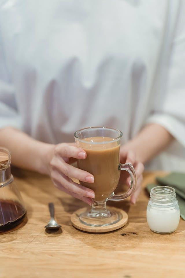 Mains de femme tenant une coupe de café au lait avec un eptit pot de lait et une cafetière