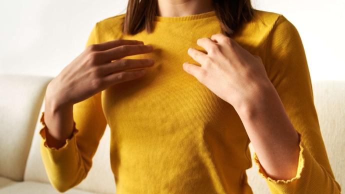 Buste femme tee-shirt jaune manche longue qui pose ses mains au-dessus de sa poitrine