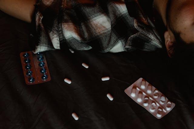 Homme brun chemise à carreaux allongé à côté de plaquettes de médicaments