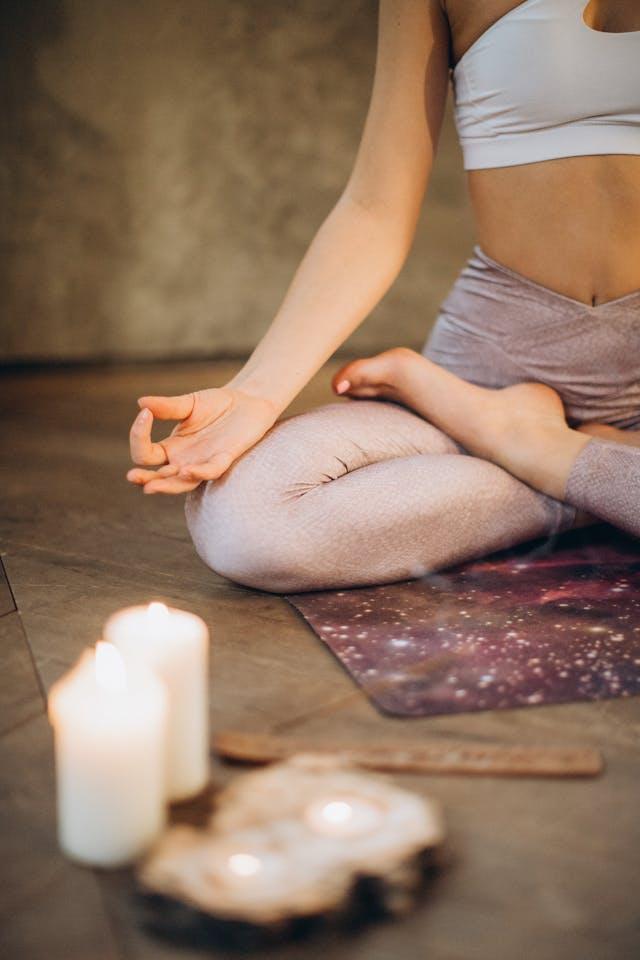 Femme en tailleur avec brassière balnche et legging beige qui médite avec deux bougies blanches allumées au premier plan