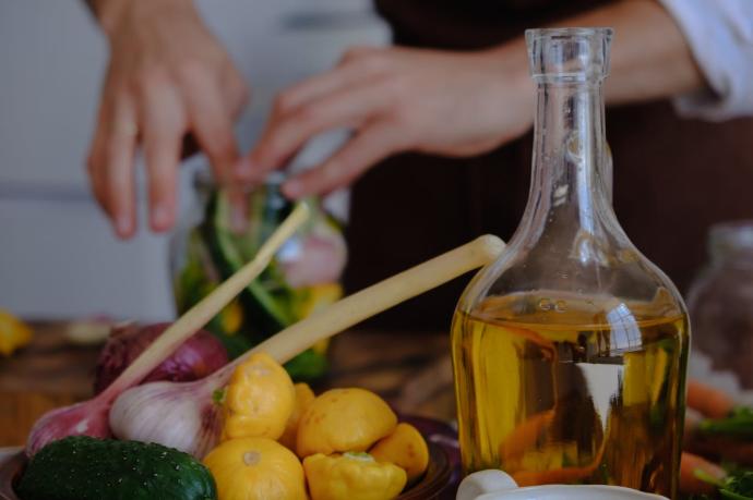 Bouteille d'huile d'olive à côté de légumes et oignons et mains d'homme à l'arrière-plan