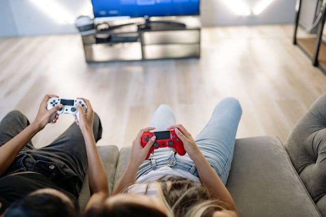 Deux jeunes allongs sur un canapé qui tiennent une manette de jeu vidéo devant une télé