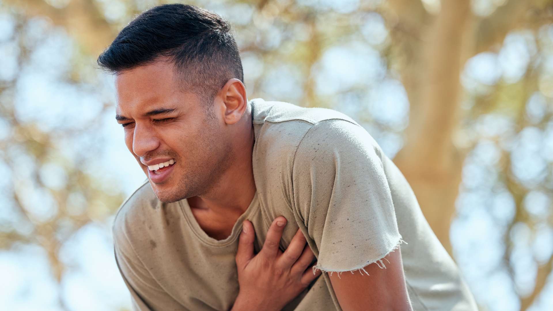 Jeune homme run peau mate en tee-shirt beige qui se tient le cœur avec la main et souffre