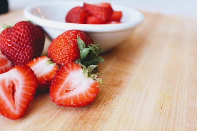 Fraises entières et coupées sur une table et dans une coupelle blanche