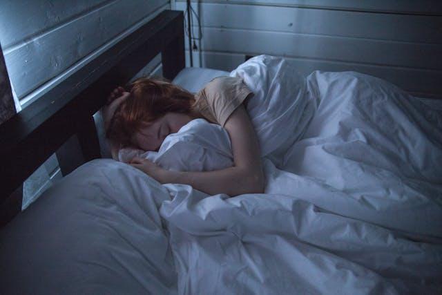 Jeune femme qui dort profondément sur le côté dans une couette blanche
