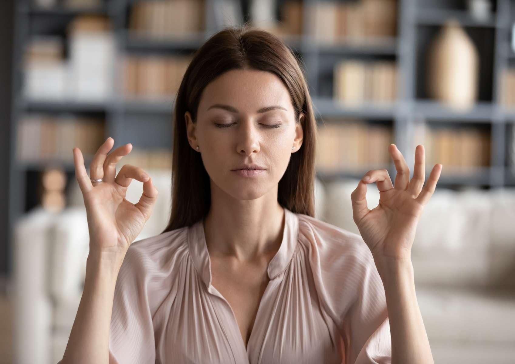 Jeune femme cheveux longs chemisier rose pâles qui médite pour se relaxer en fermant les yeux
