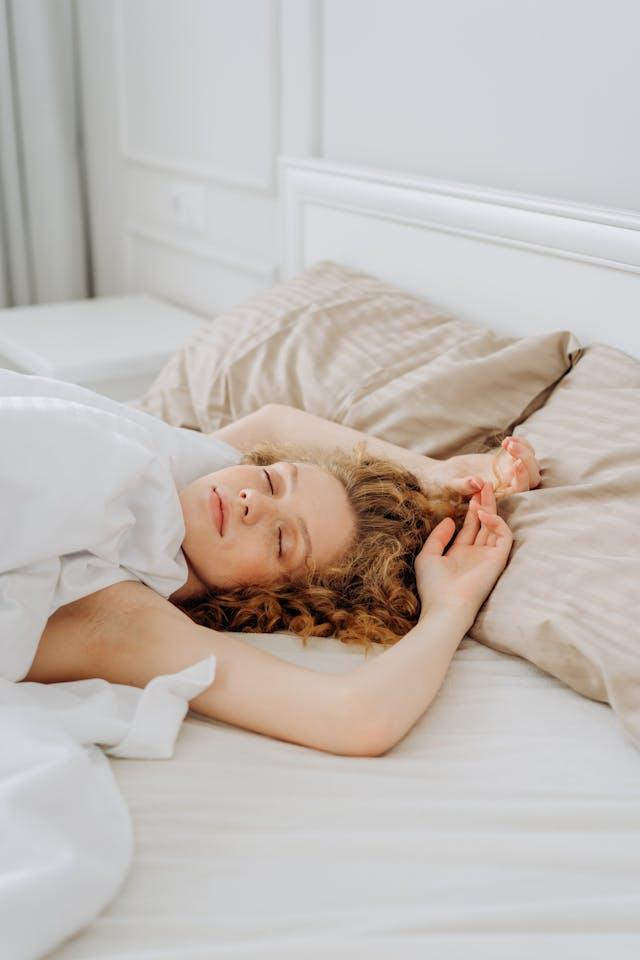 Jeune femme qui dort paisiblement les bras au-dessus de la tête dans des draps blancs