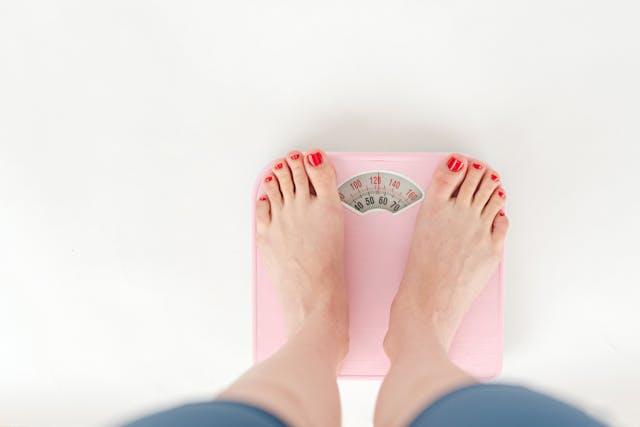 Pieds de femme avec vernis rouge sur balance rose qui indique 56 kilos