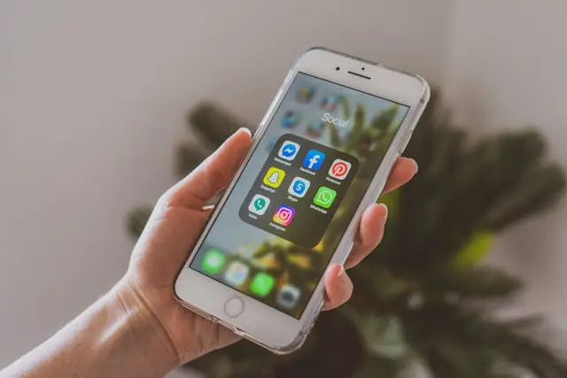 Main de femme qui tient un téléphone avec icônes applications réseaux sociaux