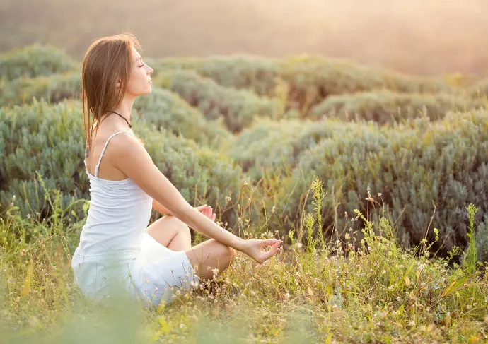 Femme qui médite en tailleur yeux fermés dans la nature