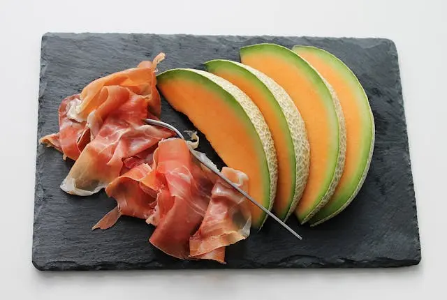 Chiffnnade de jambon cru avec tranches de melon et  fourchette sur une planche en ardoise noire
