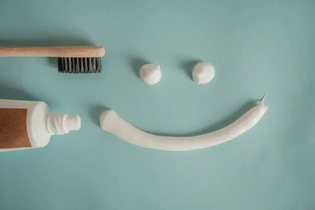 Brosse à dents et tube de dentifrice  avec dentifrice étalé pour former deux yeux et un sourire sur fond vert amande