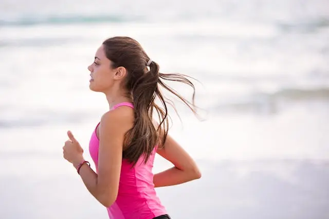 Jeune femme brune cheveux longs et débardeur rose qui court avec la mer en arrière-plan