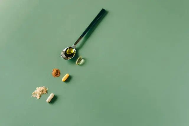 Vue de haut trois compléments alimentaires avec poudre et cuillère argentée avec liquide dedans sur fond vert moyen