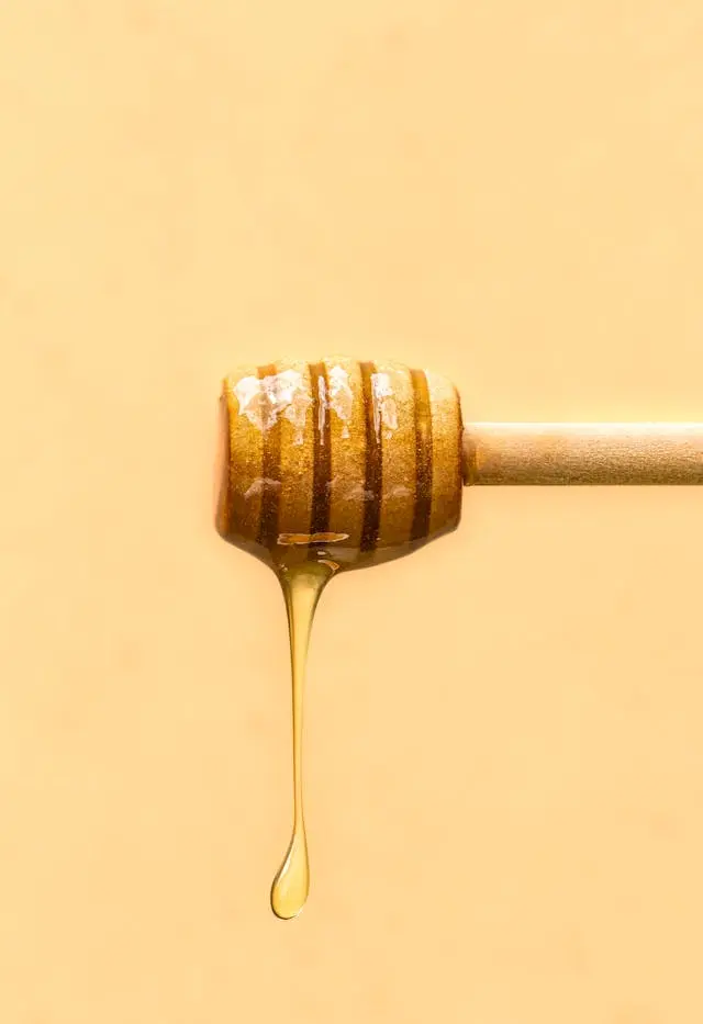 Miel qui goutte d'une cuillère en bois ronde sur fond jaune-orangé