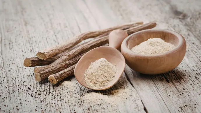 Gros plan bâtons de réglisse et poudre de réglisse dans cuillère et coupelle en bois sur table en bois clair